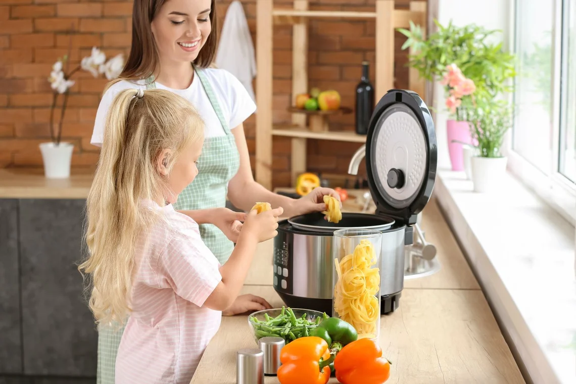 Frau und Kind kochen gemeinsam mit einem Multikocher in der Küche.