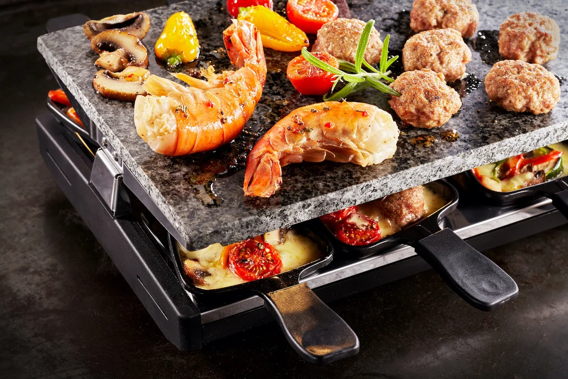 Ein Raclette-Grill mit Natursteinplatte auf dem Tisch.